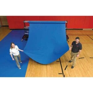 GymGuard pre-cut gym floor cover in royal blue being unrolled from a storage rack onto a wood gym floor